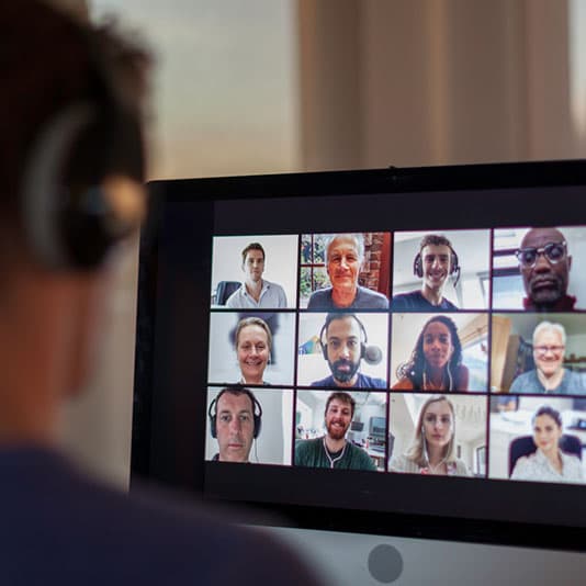 Person in headphones watching computer screen showing group of people