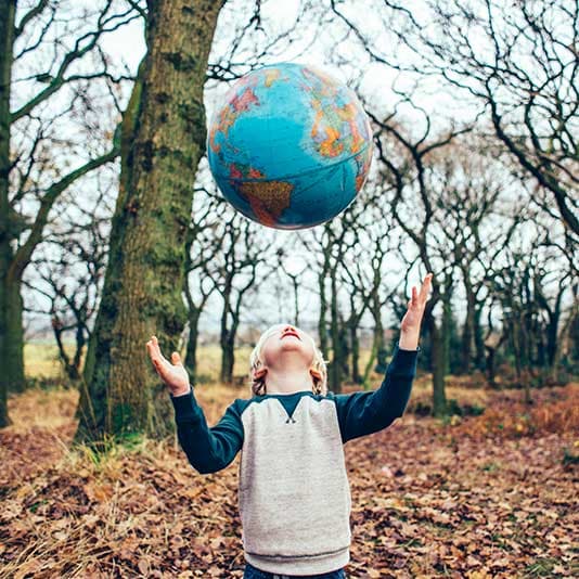 Child stood in a forest throwing a globe ball into the air