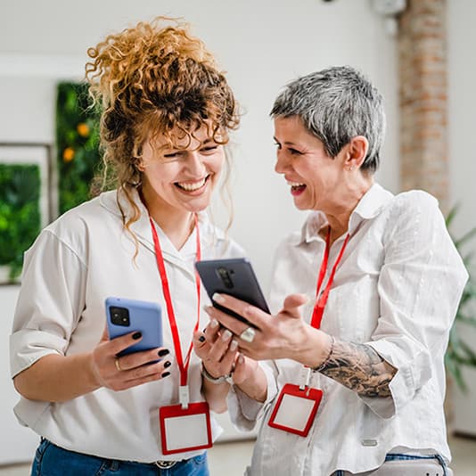 Two colleagues smiling together at work while looking at their phones