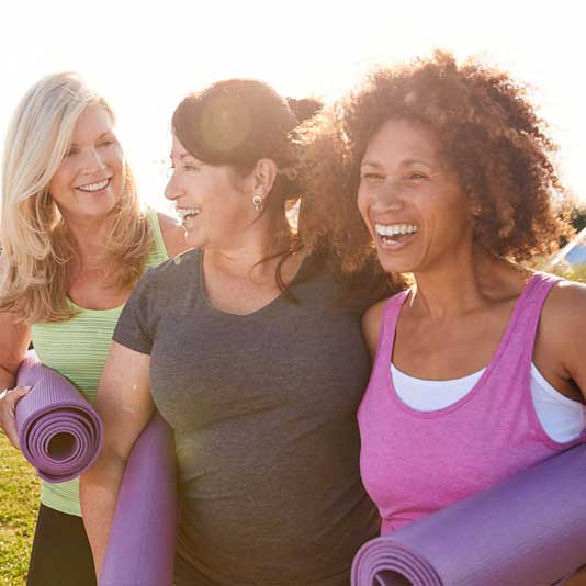 Ladies with yoga mats smiling together outside