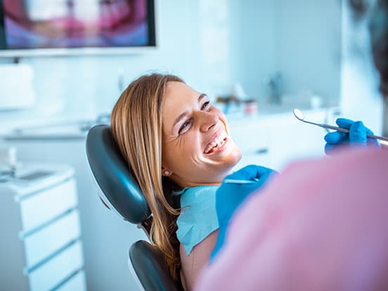 A woman smiling in a dental chair, wearing a bib, while a dentist holds a dental mirror