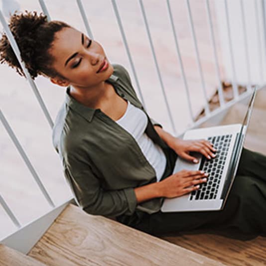 Woman sat on stairs with her laptop resting her eyes