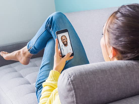 Woman sat on sofa having video GP call on smart phone