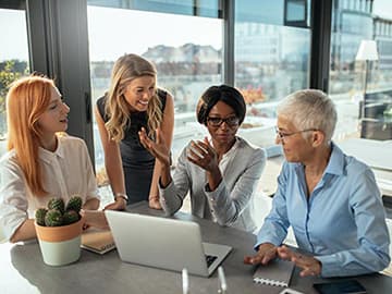 A group of women gathered around an office desk and talking