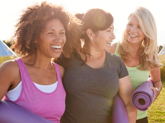 Three women walking with yoga mats and laughing